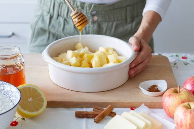 Unrecognizable person adding fresh honey to cut apples in baking pan near flour with lemon and butter with cinnamon during crumble preparation at home Copyright: xLeirexGamboax Model Released