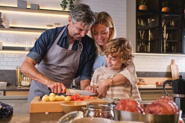 Cheerful parents and son smiling and hugging each other while peeling fresh tomato during lunch preparation in kitchen at home, Model released, Property released Copyright: xPhilippexDegrootex MR