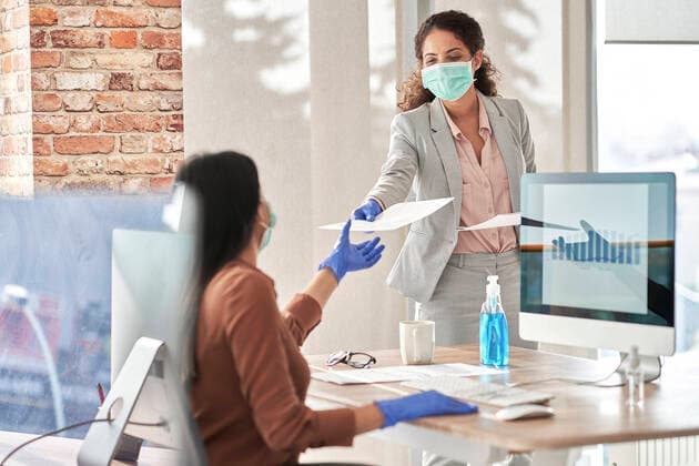 Young businesswoman giving report to female coworker while working in office during pandemic model released Symbolfoto ABIF01313