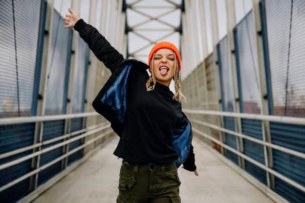 Happy young woman with eyes closed sticking out tongue while dancing on footbridge model released Symbolfoto ACPF00989