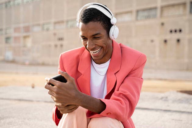 IMAGO Creative: Clickbait, Modetrends Happy man wearing headphones using mobile phone while sitting outdoors model released Symbolfoto AFVF07894