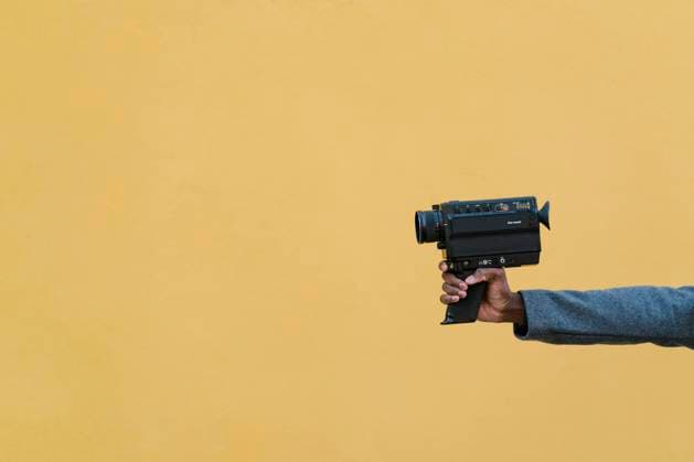 Man holding 1980s camera against yellow wall model released Symbolfoto EGAF01345