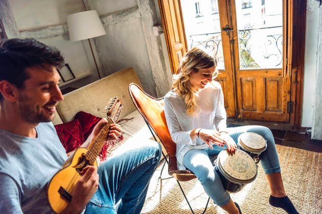 Happy young couple playing duet with drums and guitar in living room at home model released Symbolfoto property released EHF00963