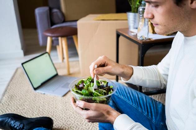 Young man with laptop having salad in living room of new loft apartment model released Symbolfoto property released GIOF10310