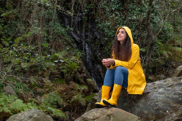 Thoughtful hiker wearing raincoat sitting on rock in forest model released Symbolfoto KBF00670