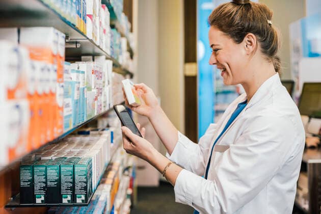Happy pharmacist with smart phone checking medicine while working at pharmacy model released Symbolfoto property released MFF06804