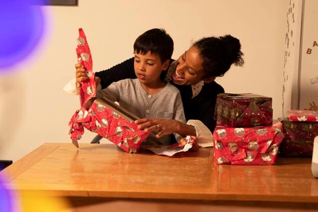 Diversity, Weihnachten Cheerful mother with son unwrapping Christmas presents on table at home model released Symbolfoto property released PMF01729