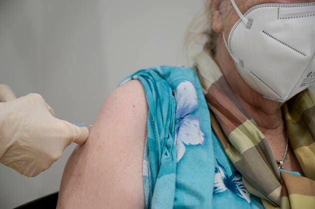 DEUTSCHLAND, Hamburg, Corona Pandemie, Impfzentrum der KVH und Sozialbehörde Hamburg in den Messehallen, groesstes Impfzentrum Deutschlands fuer bis zu 7000 Menschen taeglich, Impfung von alte Frau mit FFP2 Maske in der Impfkabine, Impfstoff Comirnaty EL 1491 von Biontech Pfizer, Hamburg Germany