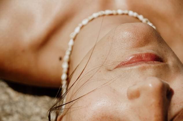 IMAGO Creative: Clickbait, Hautpflege und Kosmetik From above of crop unrecognizable peaceful young female sunbathing with closed eyes while lying on sandy beach with seashell beads on face Copyright: xMariannaxJaszczukx Model Released