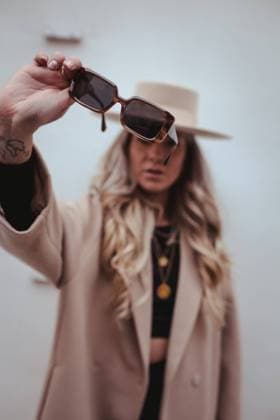 Blurred unrecognizable female influencer with long blond hair and in stylish outfit with hat and sunglasses standing with outstretch arm Copyright: xAnaxCarpiox Model Released