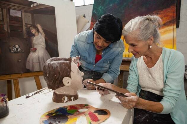 IMAGO Kreativ: Bildung, Kunsterziehung Woman using digital tablet while painting a sculptor Woman using digital tablet while painting a sculptor in drawing class, model released, , property released, Cape Town, South Africa, 21.04.2017, 1059499.jpg, craftsperson, profession, professional, painter, occupation, artist, skill, expertise, potter, pottery, senior woman, active, casual clothing, drawing class, drawing, activity, standing, holding, learning, education, practice, practicing, painting, paint, digital tablet, tablet computer, tablet pc, touchscreen, wireless technology, communication, artwork, palette, paintbrush, ideas, creative, creativity, hobby, sculptor, ceramic, art, craft, art and craft, modern, leisure, lifestyle 60s, Senior, Elderly, Woman, Female, Caucasian, 50