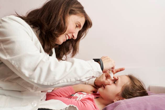 Female doctor smiling and giving eye drops to a little girl in her bed. Home doctor concept Pamplona, NC, Spain CR_SEBO210222A-580170-01 ,model released, Symbolfoto