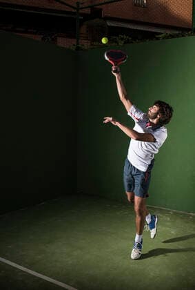 Male athlete servicing ball while playing padel tennis in sports court at night model released Symbolfoto DAMF00669
