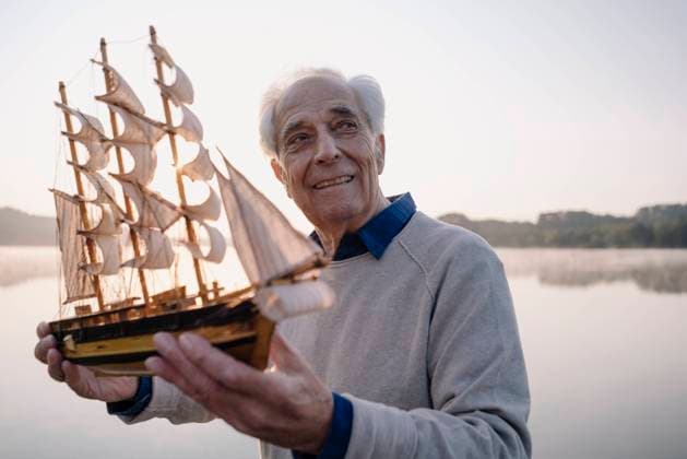Smiling man with toy boat looking away while standing against sky model released Symbolfoto GUSF05140
