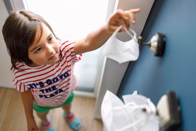 Cute girl removing protective face mask from hook at home during pandemic model released Symbolfoto property released IFRF00387