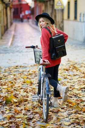Smiling woman wearing hat standing with bicycle on dry leaves over road during autumn model released Symbolfoto JSMF01922