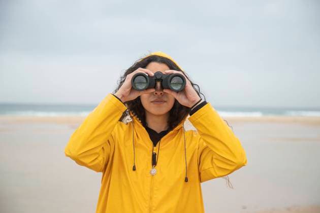 Woman using binoculars while standing at beach model released Symbolfoto KBF00703