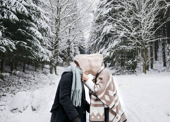 IMAGO Creative: Countdown bis Weihnachten, Nach Hause reisen Romantic couple covering face with scarf while standing on snow in forest model released Symbolfoto KMKF01521