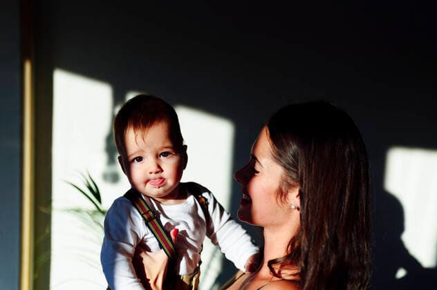 Smiling mother carrying baby boy sticking out tongue while standing at home model released Symbolfoto property released PGF00447