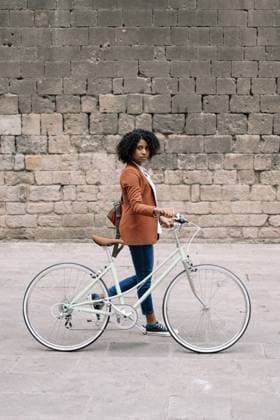 Side view of black woman in smart casual style walking along street with bike and looking at camera Copyright: xEduxFigueresx Model Released