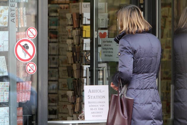 Sign with inscription Pick-up station Orders can be picked up from 10 a.m. to 1 p.m. stands on a table in the entrance area of a closed shop in the city centre of Hofheim, Hesse, Germany A customer handing over her pre-ordered goods in front of the door