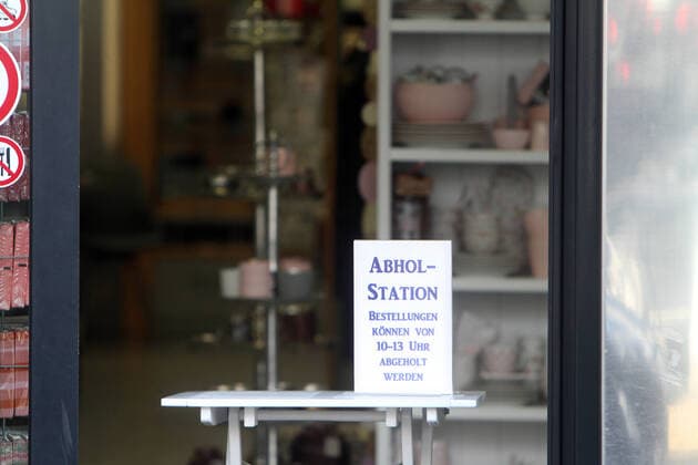 Sign with inscription Pick-up station Orders can be picked up from 10 a.m. to 1 p.m. stands on a table in the entrance area of a closed shop in downtown Hofheim, Hesse, Germany