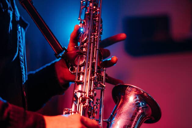 Tag der Musik am 21. Juni Crop faceless professional musician playing saxophone with fingers on keys during live concert in neon lights, Model released Copyright: xOierxAsox MR