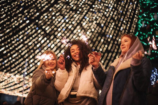 Happy female friends holding sparklers standing by Christmas lights CR_DMBE210315-652194-01 ,model released, Symbolfoto