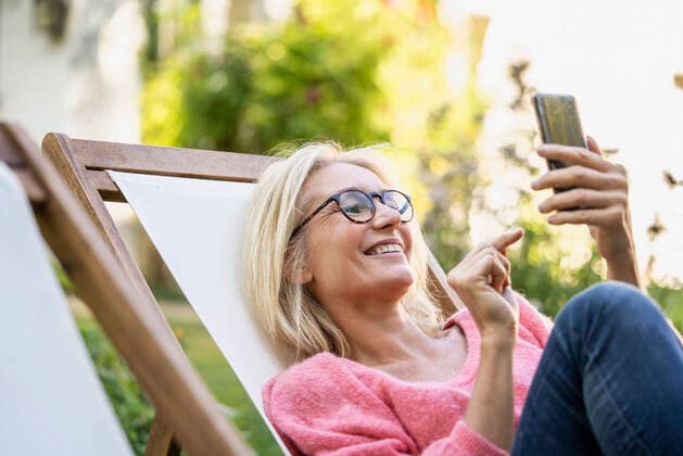 IMAGO Creative: Digitale Welt, Social Commerce Smiling mature woman using smartphone while sitting on deckchair Copyright: FrédéricxCirou B56005745