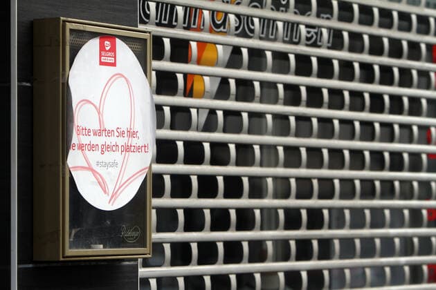 A sticker from last summers relaxation still hangs on a restaurant closed with a roll-up door Please wait here, you are about to be placed in downtown Frankfurt, Hesse, Germany