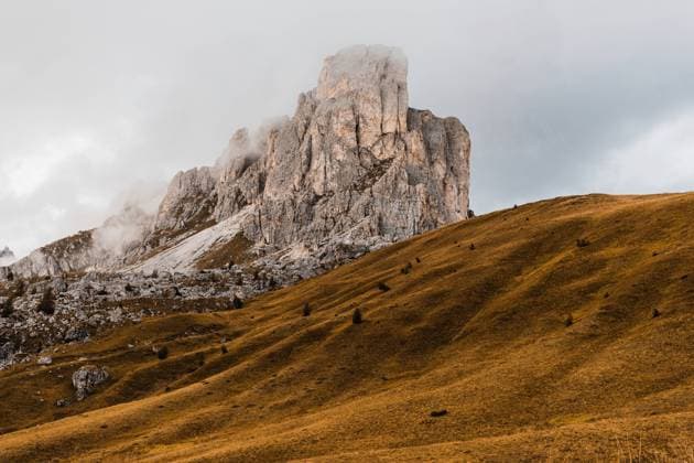 Creative Highlights World Picturesque scenery with rough steep rocky peak and hills covered with yellow grass under clouds in Dolomites mountain range in Italy Copyright: xAdrianxVilanovax Model Released