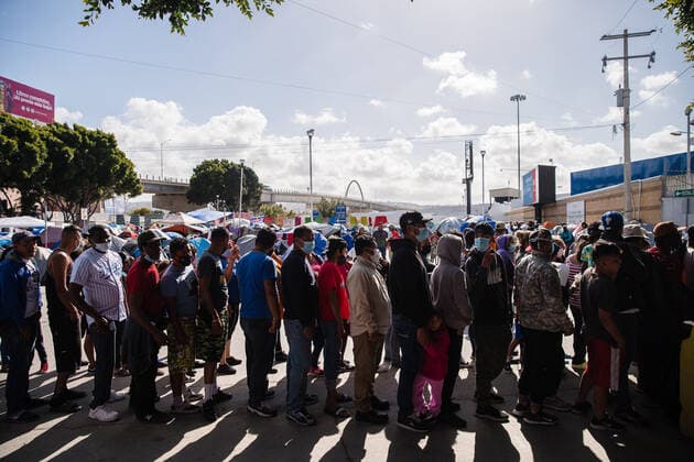 Asylum Seekers wait in line for food near El Chaparral plaza in Tijuana, Mexico on Sunday, March 21, 2021. Hundreds of asylum seekers have set up tents near the port of entry in hopes of being able to seek asylum in the United States. Biden has pledged to take new steps to address the surge of migrants on the border since he took office.  TIJ2021032118 ARIANAxDREHSLER