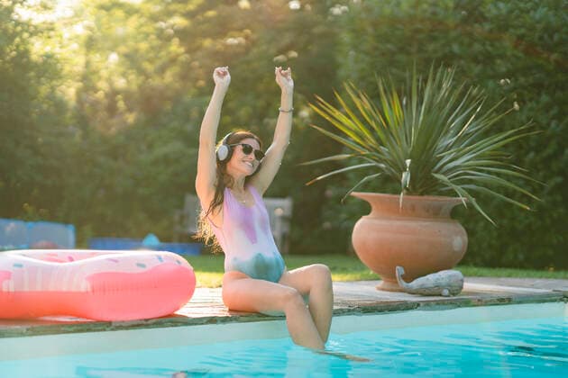 Cheerful woman in swimwear enjoying music while sitting at pool model released Symbolfoto property released AKLF00065