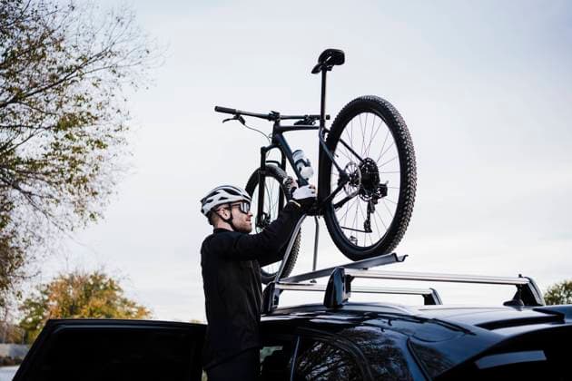 IMAGO Creative: Fit durch den Herbst Male cyclist keeping bicycle on top of car against sky model released Symbolfoto EBBF02513