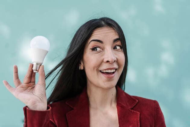 Surprised businesswoman holding light bulb against turquoise wall model released Symbolfoto JCZF00494