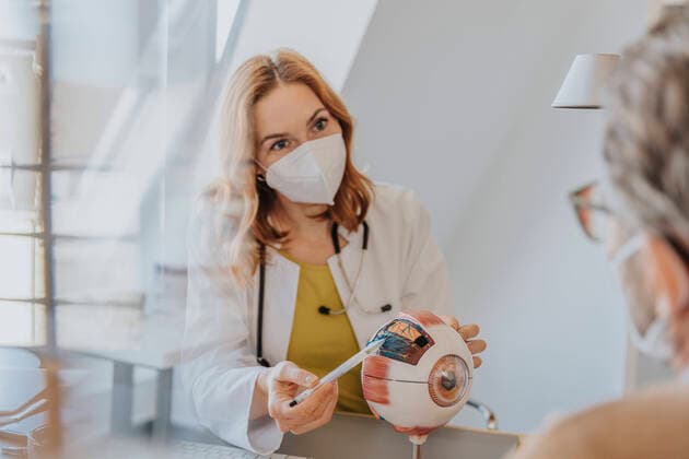 Doctor with protective face mask explaining patient over eye model at clinic model released Symbolfoto property released MFF07575