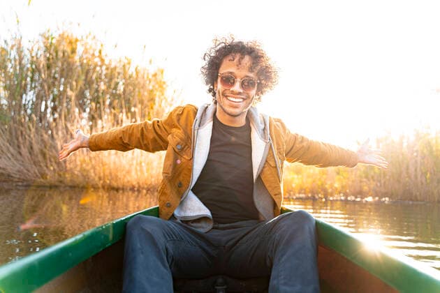 IMAGO Creative: Neue Frühlingsmode Smiling man sitting with arms outstretched in canoe on river model released Symbolfoto SBOF02681