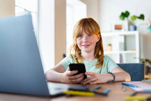 Smiling redhead girl holding smartphone and looking at laptop in living room model released Symbolfoto property released SBOF03029