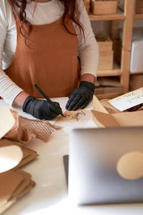 Female entrepreneur writing thank you note to put it in order packaging at workshop model released Symbolfoto property released VEGF03992