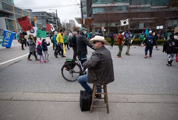 March 27, 2021, Vancouver, BC, Canada: A man wearing a cowboy hat sits on a stool with a cigarette in his mouth as he watches people taking part in an Extinction Rebellion protest against old-growth logging march past, in Vancouver, B.C., Saturday, March 27, 2021. The group of protesters marched onto the Cambie Bridge forcing the closure of all lanes of traffic into and out of downtown. Vancouver Canada  - ZUMAc35_ 20210327_zaf_c35_058 Copyright: xDarrylxDyckx