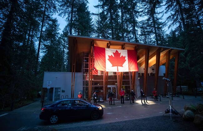 April 3, 2021, North Vancouver, BC, Canada: A motorist drives past a colour guard under a Canadian flag during a drive-thru candlelight vigil for the victims of last week s mass stabbing incident in and around the Lynn Valley Library, at Lynn Canyon Park in North Vancouver, B.C., on Saturday, April 3, 2021. North Vancouver Canada  - ZUMAc35_ 20210403_zaf_c35_089 Copyright: xDarrylxDyckx