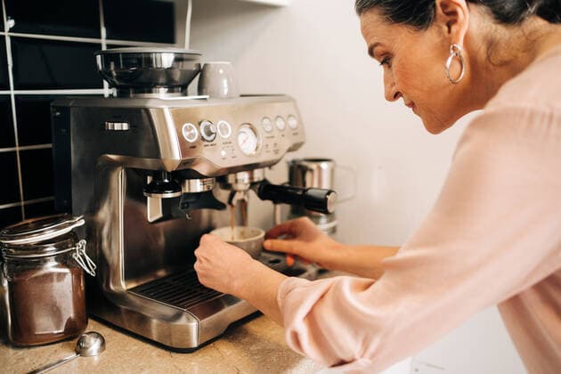 IMAGO Creative: Haushaltsger?te - Kaffeemaschine Side view of concentrated middle aged female preparing fresh coffee while using modern coffee maker at kitchen counter, Model released Copyright: xJakexJakabx MR