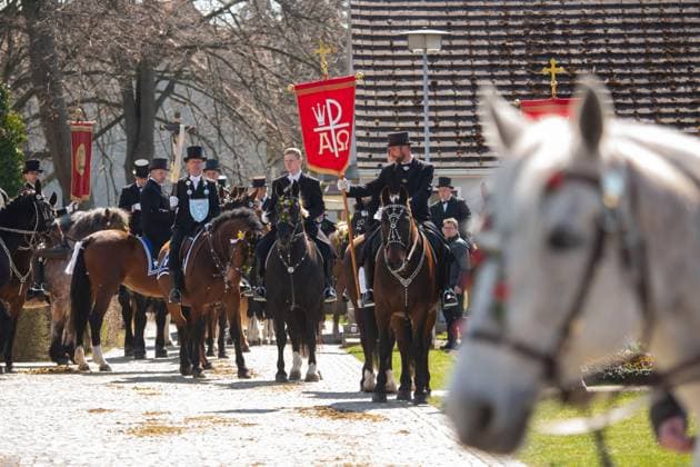 Hoch zu Ross, mit dem Kreuz, einer Statue des Auferstandenen, reiten glaeubige Katholiken waehrend des Osterreitens am 04.04.2021 in Ralbitz in Ostsachsen. Jedes Jahr am Ostersonntag schwingen sich Scharen von Reitern in den Sattel und verkuenden vom Pferderuecken aus die christliche Osterbotschaft, dass Jesus von den Toten auferstanden ist. Nach einer hundertjährigen Tradition reiten sorbische Maenner, meist in einem schwarzen Frack gekleidet, auf geschmueckten Pferden und verkuenden, singen und beten die Botschaft der Auferstehung Jesu. Die Sorben sind eine slawisch-deutsche Minderheit nahe der deutsch-polnischen Grenze. Men carry banners of their parish during the beginning of the Easter riders procession om April 4, 2021. According to