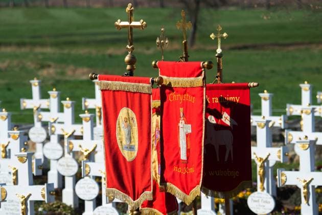 Kirchenfahnen stehen zwischen den weissen Holzkreuzen vor Beginn des Osterreitens am 04.04.2021 in Ralbitz in Ostsachsen. Jedes Jahr am Ostersonntag schwingen sich Scharen von Reitern in den Sattel und verkuenden vom Pferderuecken aus die christliche Osterbotschaft, dass Jesus von den Toten auferstanden ist. Nach einer hundertjährigen Tradition reiten sorbische Maenner, meist in einem schwarzen Frack gekleidet, auf geschmueckten Pferden und verkuenden, singen und beten die Botschaft der Auferstehung Jesu. Die Sorben sind eine slawisch-deutsche Minderheit nahe der deutsch-polnischen Grenze. Men carry banners of their parish during the beginning of the Easter riders procession om April 4, 2021. According to a more than hundred years old trad