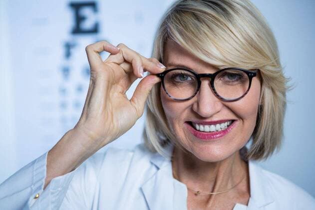 Smiling female optometrist wearing spectacles Portrait of smiling optometrist wearing spectacles in ophthalmology clinic, model released, , property released, Cape Town, South Africa, 19.06.2016, 808299.jpg, doctor, optometrist, ophthalmologist, ophthalmology, optometric, optician, oculist, job, profession, expertise, specialist, clinic, laboratory coat, spectacles, eyecare, medical, examining, examine, checking, holding, eyesight, vision, examination room, eye chart, snellen chart, alphabet, smiling, happy, cheerful, confidence, beautiful, pretty, smart 50s, Mature Adult, Woman, Female, Caucasian, 50-54 Years, Mature Women, Caucasian Ethnicity Indoors,Portrait,Looking at camera