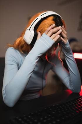 IMAGO Creative: Sport Start-Up Side view of worried female gamer in headphones playing video game while sitting at table with keyboard Copyright: xDanixNavarrox Model Released