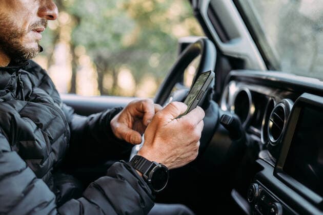 Crop view of unrecognizable man using his mobile inside the car before starting to drive, Model released Copyright: xMarcosxOsoriox MR