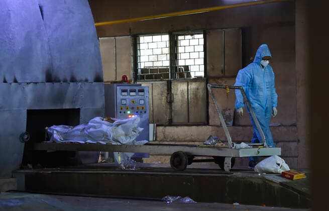 NEW DELHI, INDIA - APRIL 22: A relative of a Covid-19 victim in PPE coveralls performs the last rites, at Nigambodh Ghat crematorium, on April 22, 2021 in New Delhi, India. (Photo by Ajay Aggarwal Hindustan Times) Covid Death Toll Continues To Rise In India