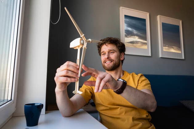 IMAGO Creative: Corporate: Klimaschutz, Digitalisierung und Urbanisierung IMAGO Creative: Klimawandel - Zukunft und Innovation Smiling businessman holding wind turbine model while sitting at home model released Symbolfoto property released VPIF03875