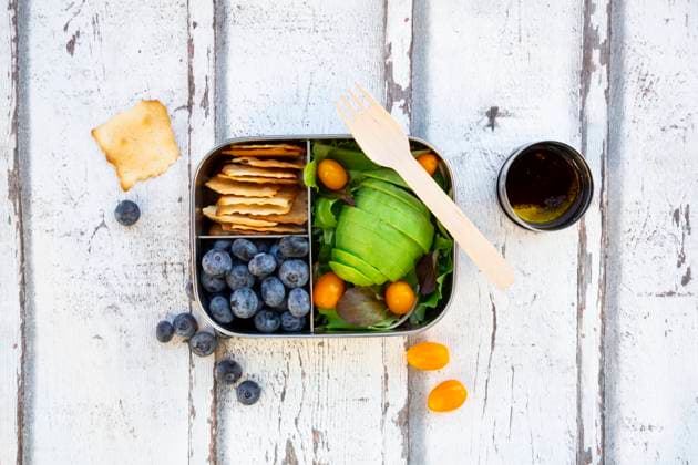 Lunchbox with salad, avocado and yellow tomatoes, crackers, blueberries and salad dressing LVF08195
